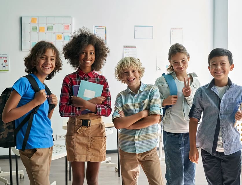 A group of diverse kids smiling and posing together in a classroom.