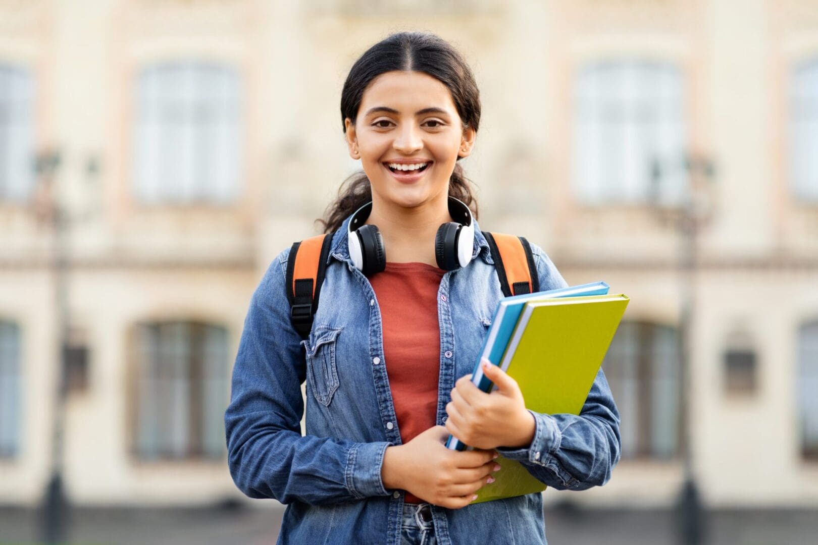 A smiling young student holding notebooks outdoors.