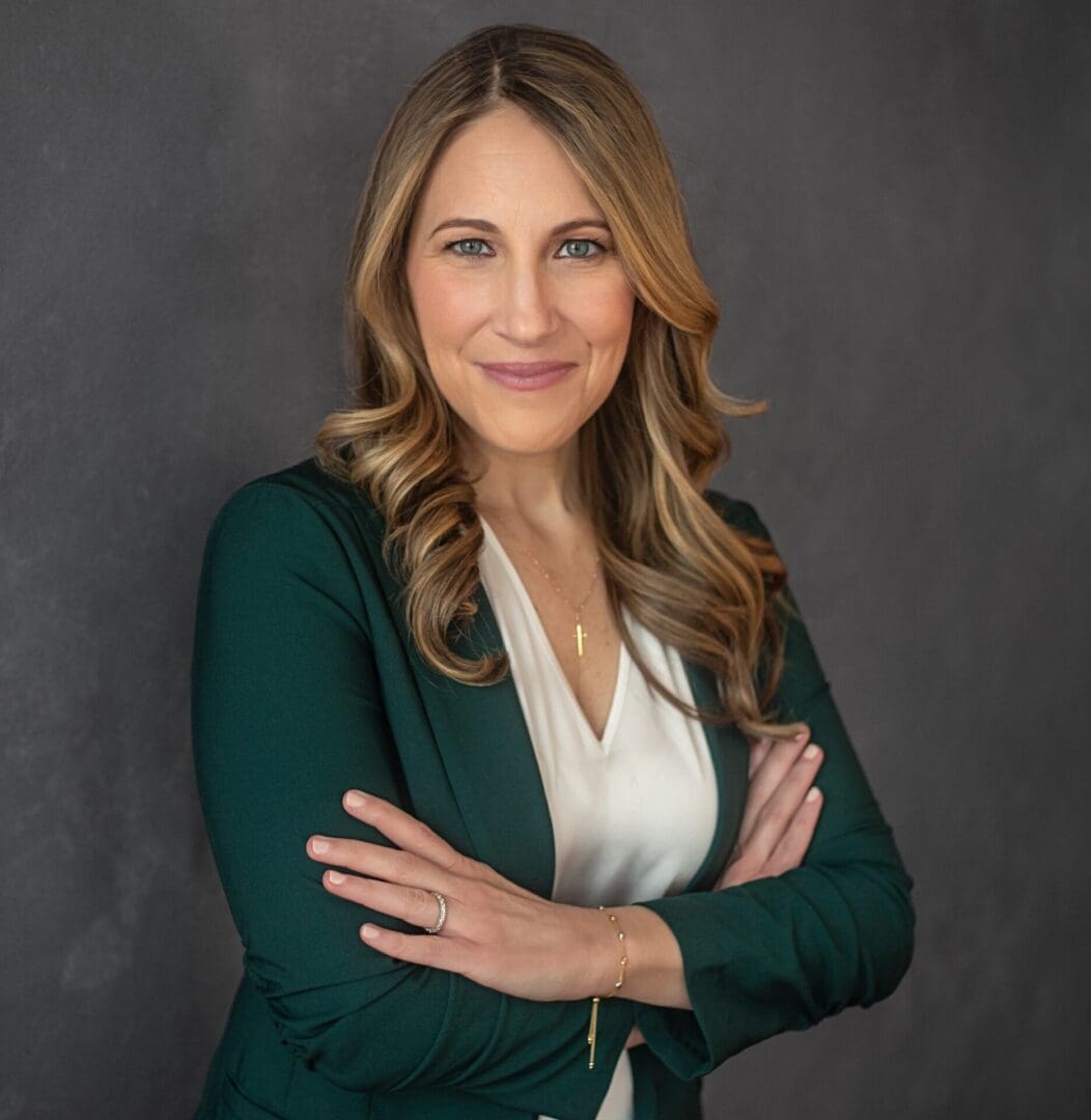 Professional woman with blonde hair, wearing a green blazer and white blouse, smiling confidently.