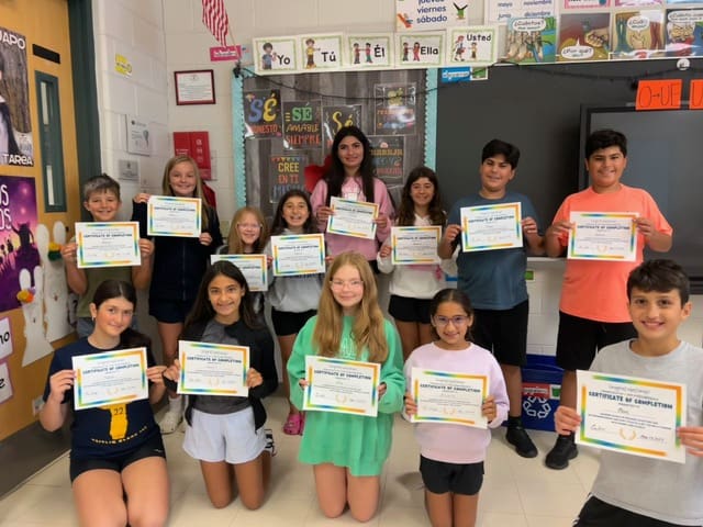 A group of children proudly holding certificates in a classroom.