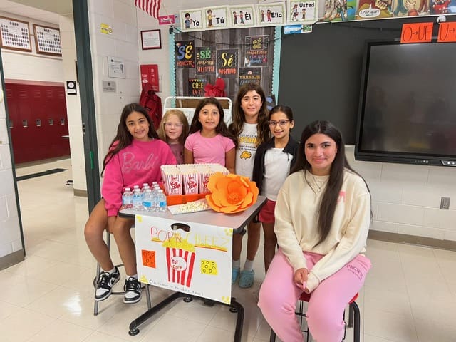 A group of young girls standing and sitting around a decorated table with bags.