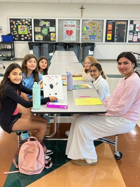 Group of six young people smiling around a classroom table with books and papers.