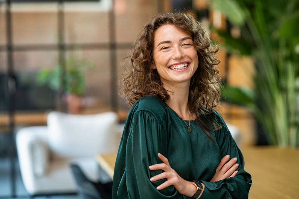 Smiling woman with curly hair in a green blouse indoors.