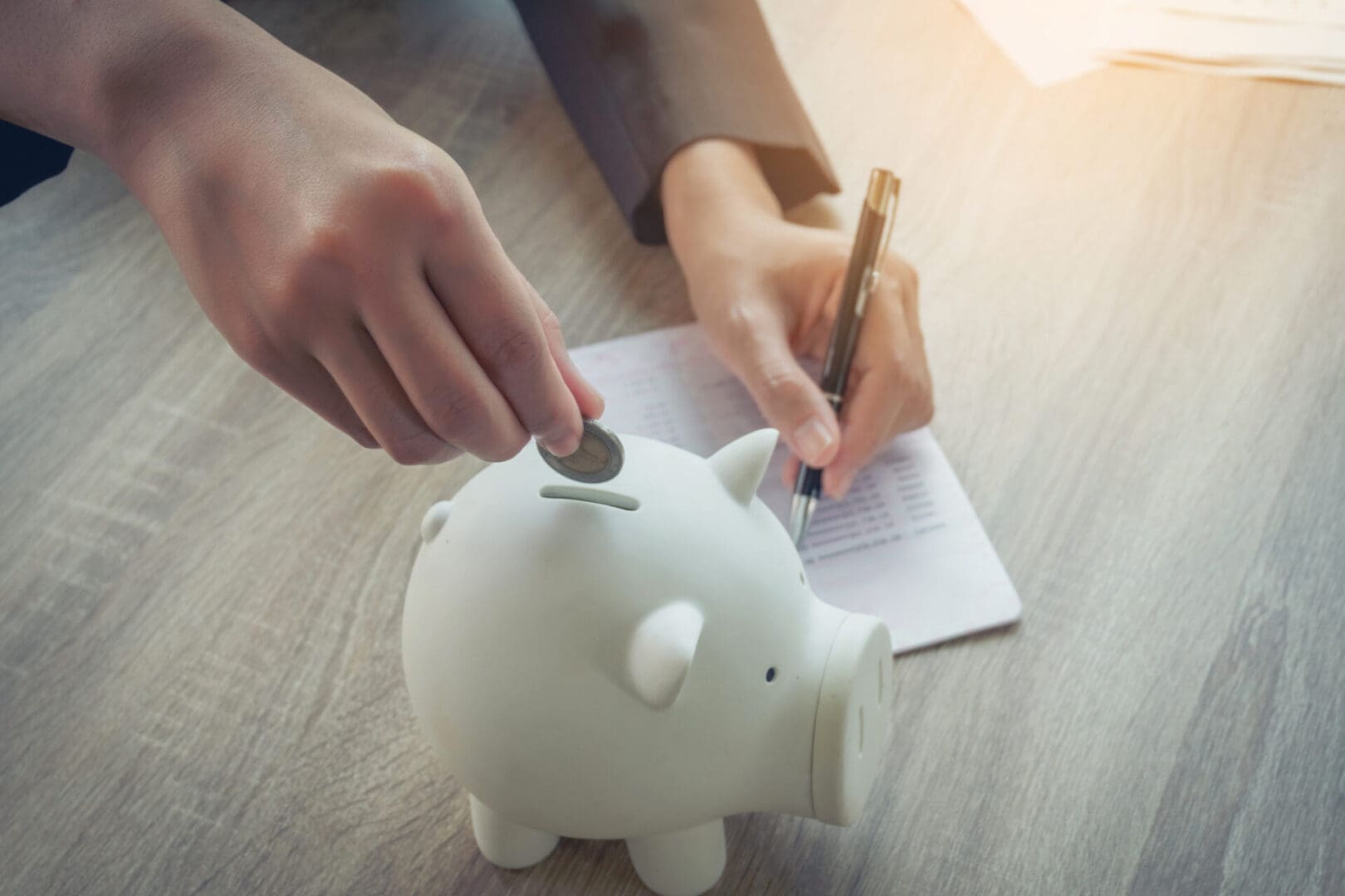 Person saving money by putting coins in a piggy bank and writing notes.