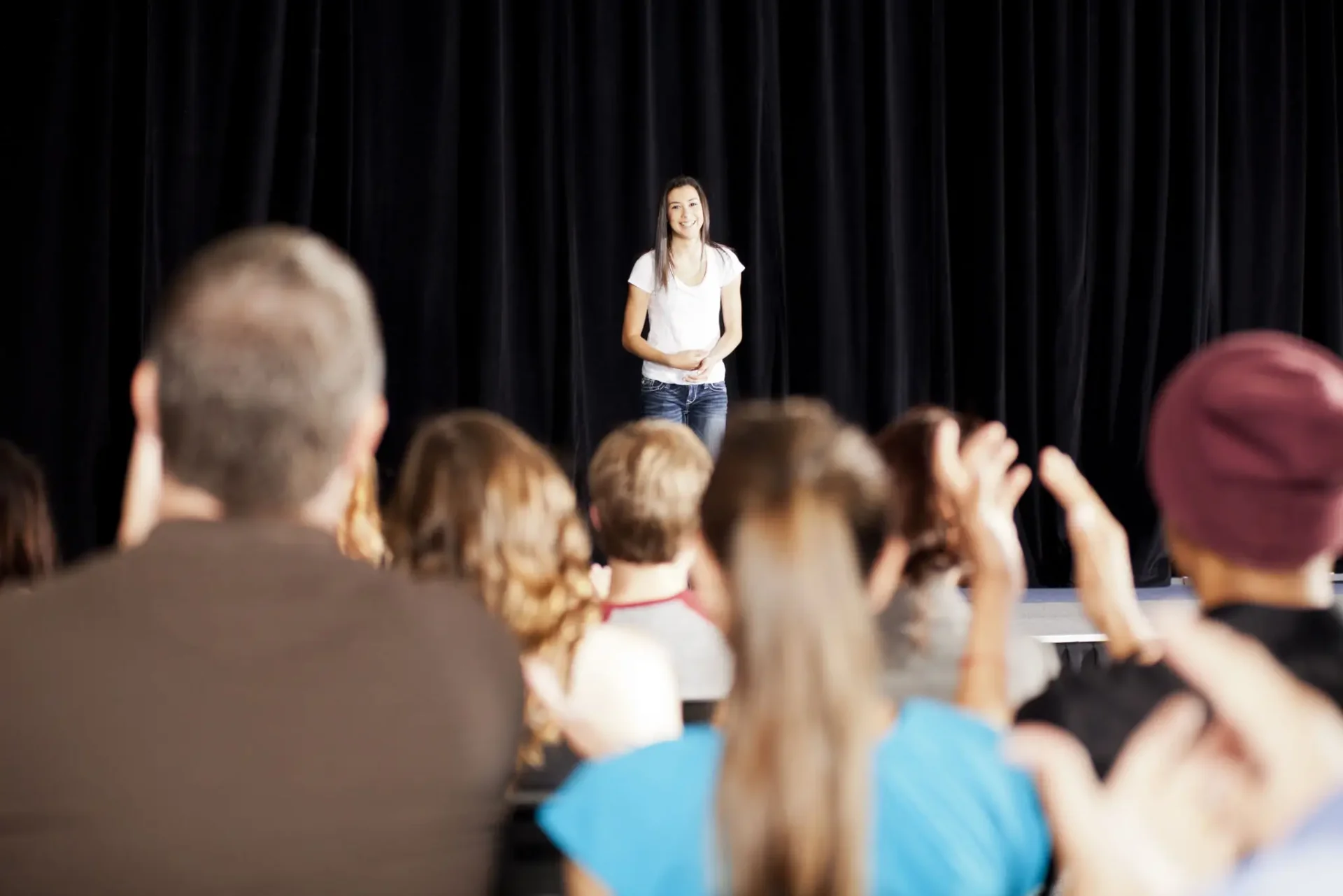 A person speaking to an attentive audience in a dark room.