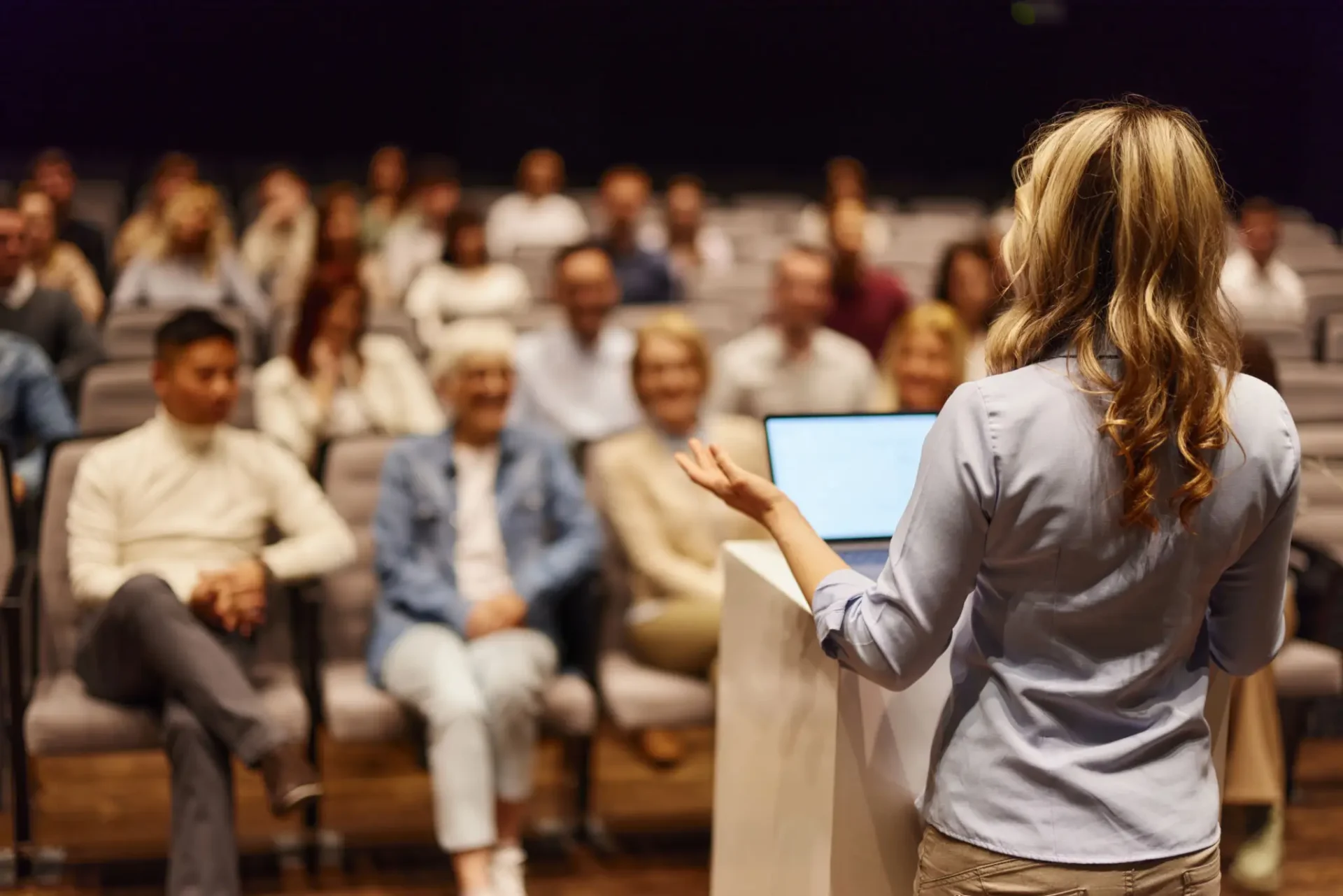 A speaker addressing a seated audience in a conference setting.