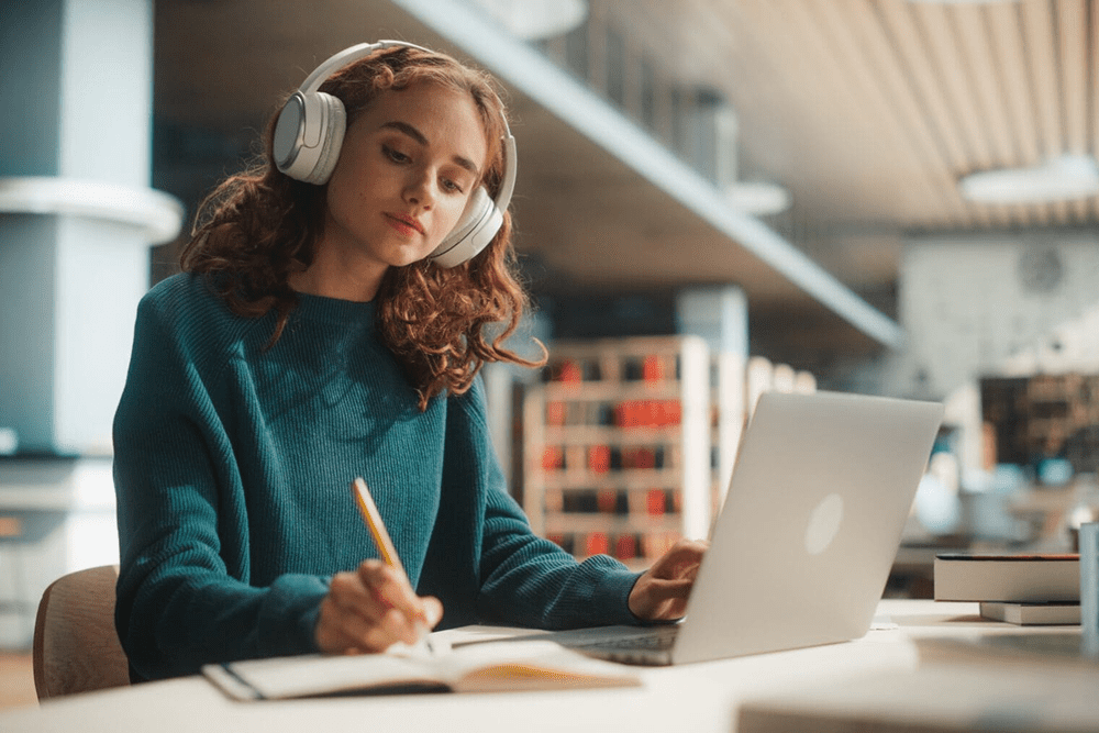 Young woman studying with headphones and laptop in a cozy room.