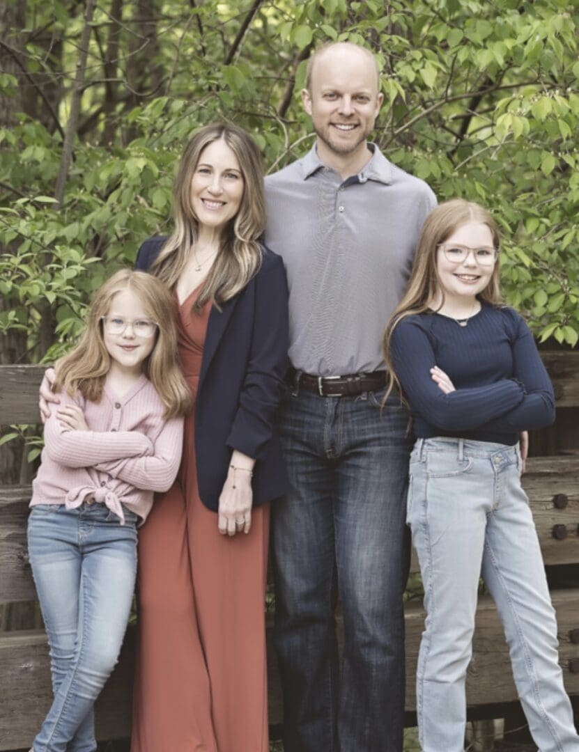 A family of four posing outdoors with greenery in the background.